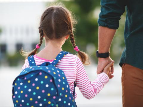 Koristekuva, lapsi pitää isää kädestä kun he kävelevät kouluun.