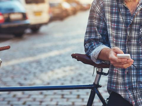 Koristekuva, aikuinen mies pyörän vieressä valitsee puhelimesta kuunneltavaksi omahoito harjoitusta. 